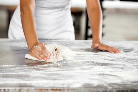 Midsection of female baker cleaning flour from table in bakeryの写真素材