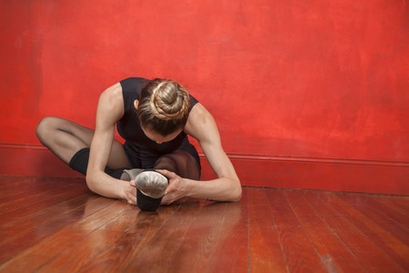 Young ballerina stretching her legs on hardwood floor in studioの写真素材