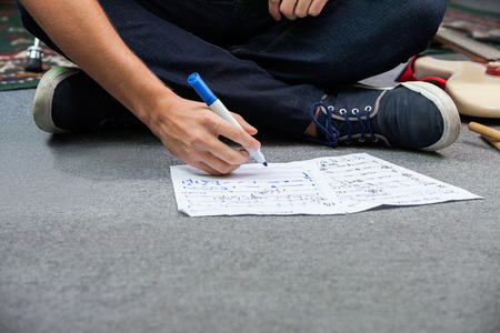 Low section of male drummer writing notes on paper while sitting on floor in recording studioの写真素材