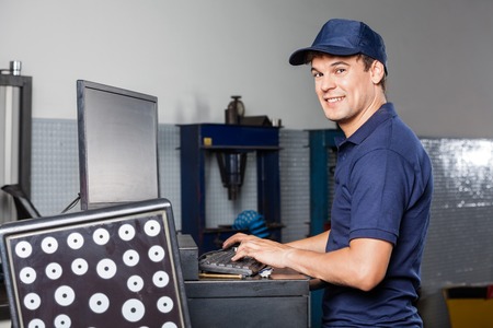Side view portrait of male mechanic using computer in auto repair shopの写真素材