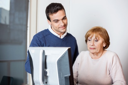 Young male teacher helping senior student at computer desk in classroom