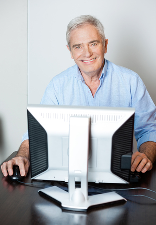 Portrait of happy senior man using computer at desk in classの写真素材