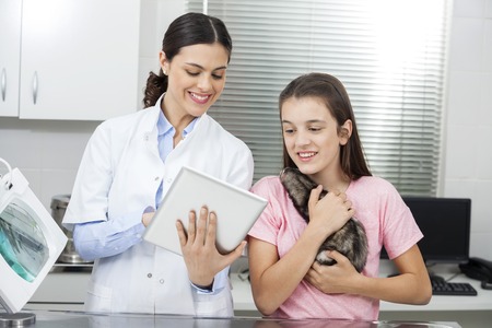 Female doctor showing tablet computer to girl holding weasel in clinicの写真素材