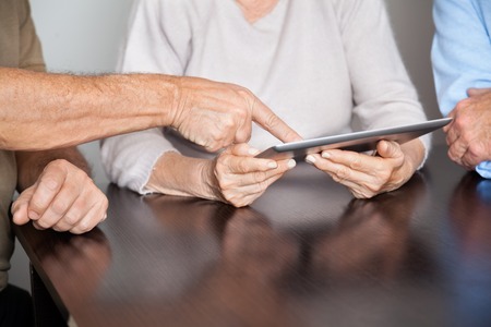 Cropped image of senior people using tablet PC at desk in computer class