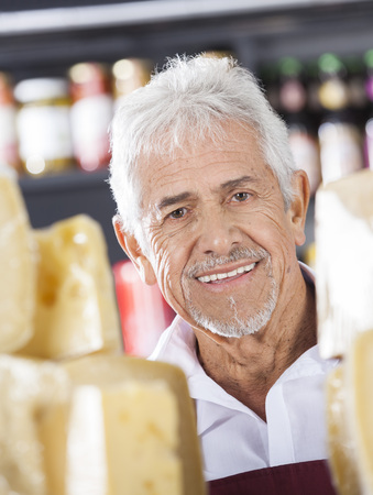 Portrait of happy senior salesman in cheese shopの写真素材