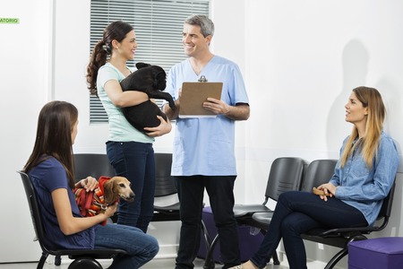 Male nurse holding clipboard while pet owners looking at him in waiting area of clinicの写真素材