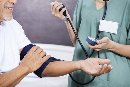 Midsection of female nurse checking blood pressure of senior patient in rehab centerの写真素材
