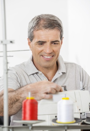 Happy mature male tailor adjusting sewing machine in factory
