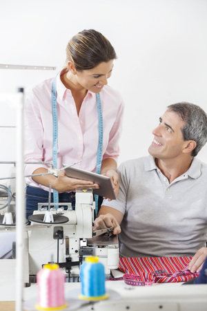 Smiling male and female tailors using digital tablet at workbench in sewing factoryの写真素材