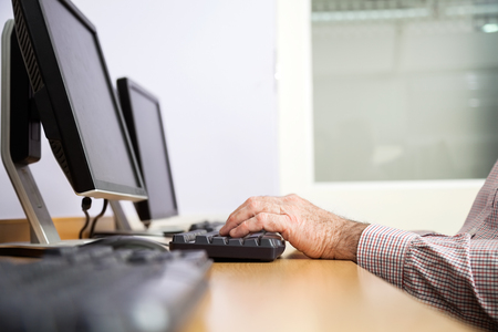 Cropped hand of senior man using computer at desk in classroomの写真素材