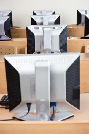 Row of computer monitors arranged on desks in classroomの写真素材
