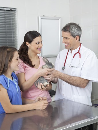Happy mature male vet receiving rabbit from family for checkup in clinicの写真素材
