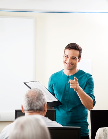 Happy young male tutor taking lecture in computer classの写真素材