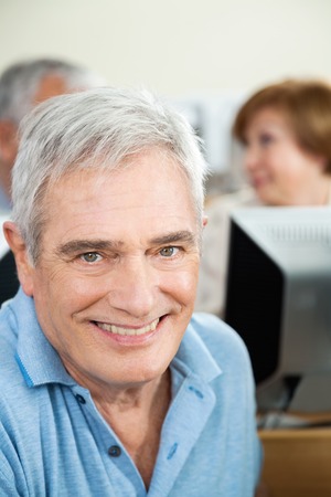 Portrait of happy senior man with classmates in background at computer classの写真素材