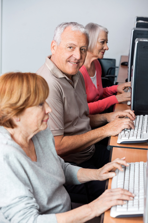 Portrait of happy senior man using computer at desk with classmates in classroomの写真素材