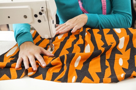 Cropped image of female tailor sewing fabric at workbench in factoryの写真素材