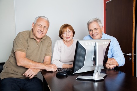 Portrait of happy senior people using computer at desk in classroomの写真素材