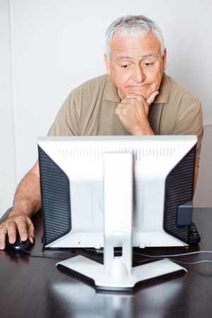Thoughtful senior man using computer at desk in classroomの写真素材