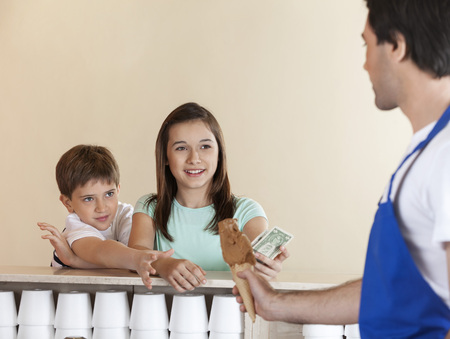 Tempted siblings paying for chocolate ice cream to waiter at parlorの写真素材