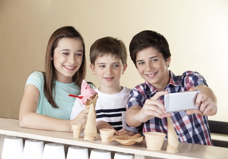Happy preteen boy taking selfie with siblings through smart phone at counter in parlorの写真素材