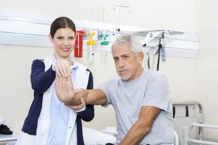 Young female doctor examining senior man's hand in rehab centerの写真素材