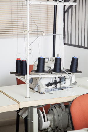 Black thread spools and sewing machine on workbench at factoryの写真素材