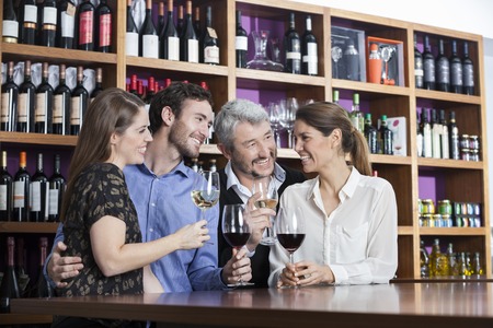 Happy male and female friends enjoying wine at counter in wineryの写真素材