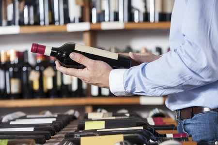 Midsection of male customer holding red wine bottle in shopの写真素材