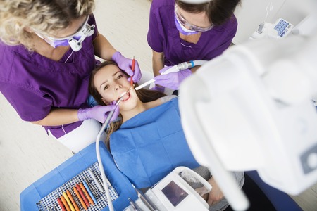 High angle portrait of young female patient being examined by dentists in clinicの写真素材