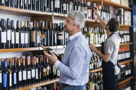 Side view of male customer and salesman choosing wine bottles in storeの写真素材