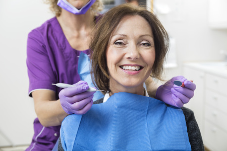 Portrait of smiling female patient with dentist holding tools in clinicの写真素材