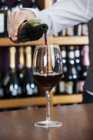 Cropped image of male bartender pouring red wine in glass at counterの写真素材