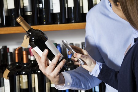 Midsection of couple scanning barcode on wine bottle through smartphone in supermarketの写真素材