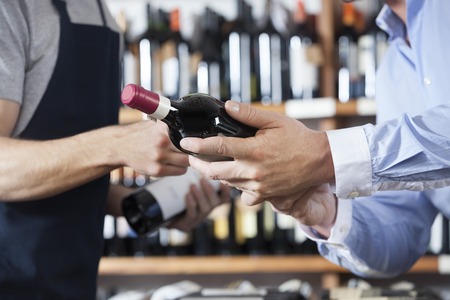 Midsection of male customer and salesman with wine bottles in shopの写真素材