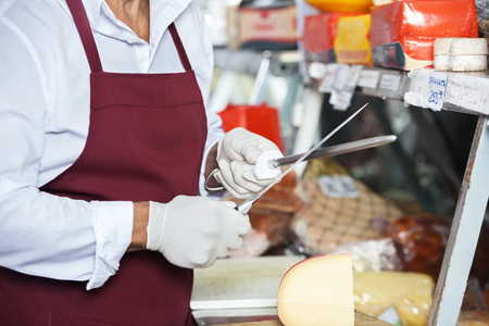 Midsection of senior man sharpening knives at counter in cheese shopの写真素材
