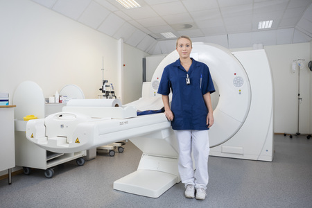 Full length portrait of young female radiologist standing by magnetic resonance imaging machine in...