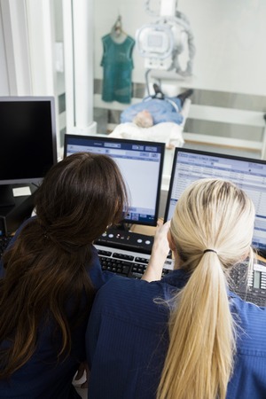 Rear view of female doctor's using computers while patient lying under xray machine in hospital