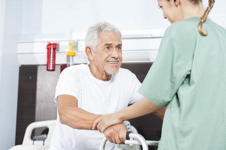 Young female nurse helping smiling senior man in using walker at hospitalの写真素材