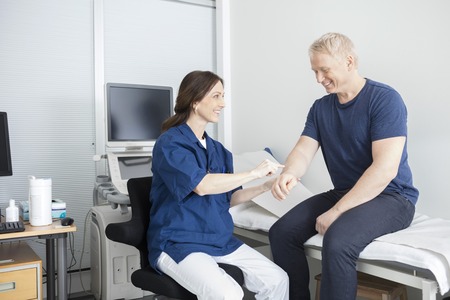 Smiling mature female doctor touching male patient's hand in clinic