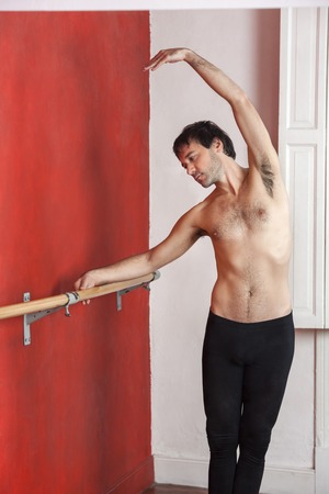 Shirtless male ballet dancer practicing at barre against wall in dance studioの写真素材