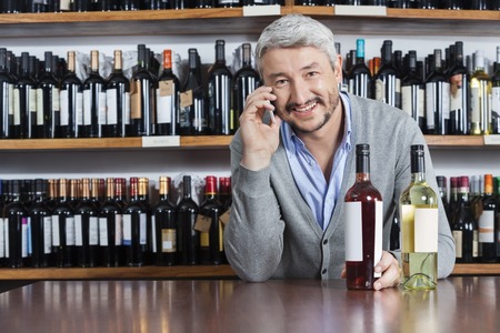 Portrait of happy customer using mobile phone in wine shopの写真素材