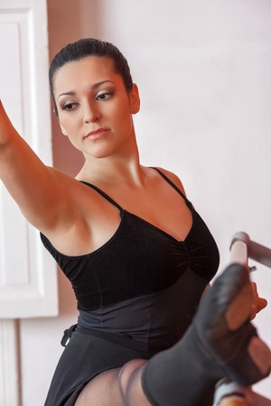 Thoughtful young ballerina practicing at ballet bar in dance studio