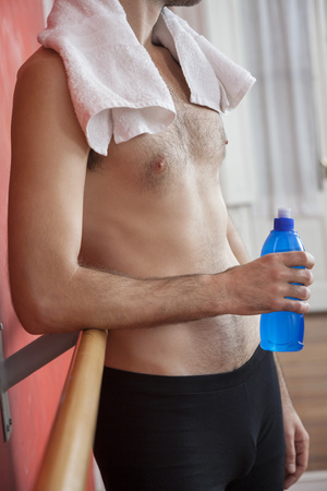 Midsection of shirtless ballet trainer holding waterbottle in dance studioの写真素材