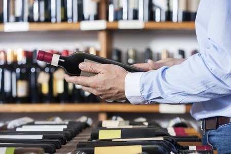 Midsection of male customer holding wine bottle in shopの写真素材