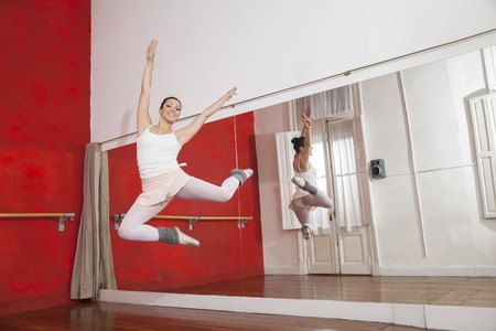Full length portrait of ballerina jumping while performing in dance studioの写真素材