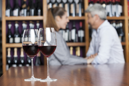 Closeup of red wine in glasses with couple in background at shopの写真素材