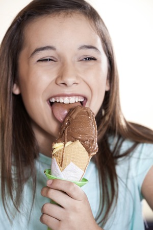 Happy girl licking delicious chocolate ice cream in parlorの写真素材