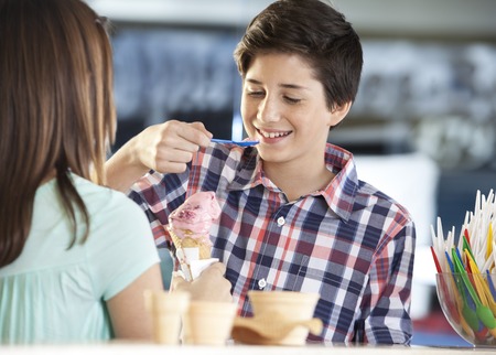 Smiling boy having strawberry ice cream while standing with sister in parlorの写真素材