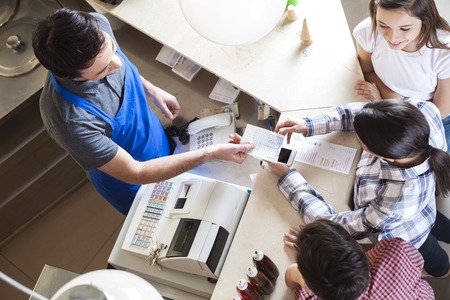 High angle view of waiter giving receipt to woman standing with family at icecream parlorの写真素材