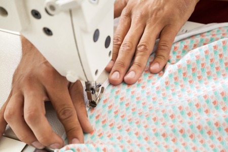 Cropped image of male tailor sewing fabric at workbench in factory